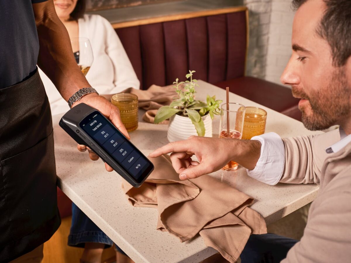 services-02 A diner uses a handheld POS system for digital tipping in a casual restaurant setting.